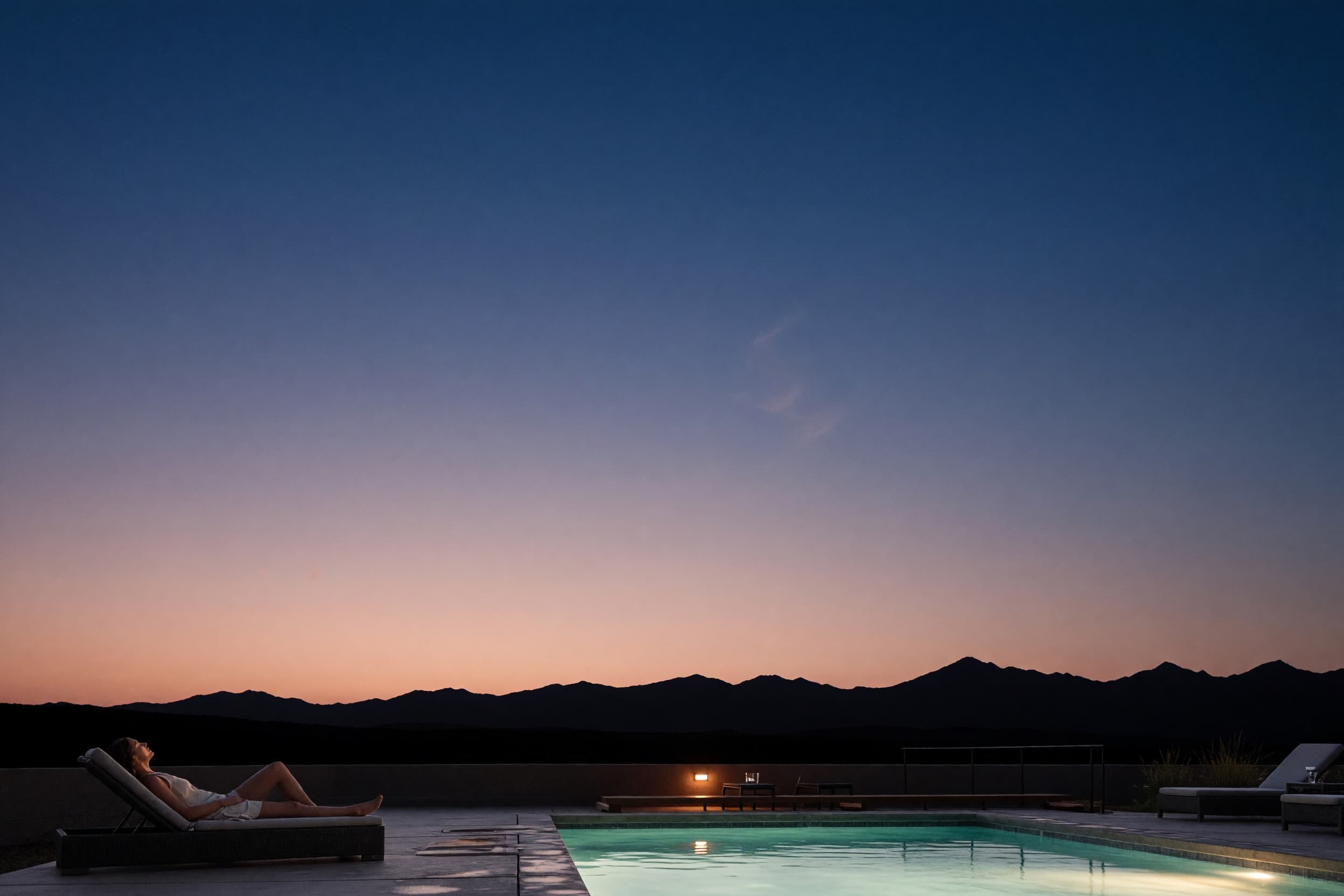 A guest reclining poolside at dusk beneath an immense Montana sky